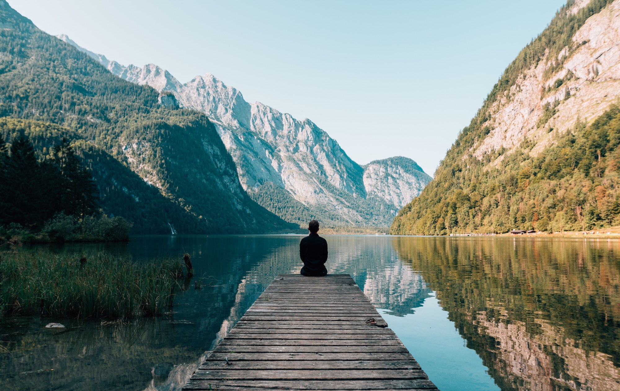 A man sitting on a dock in a serene mountain lake