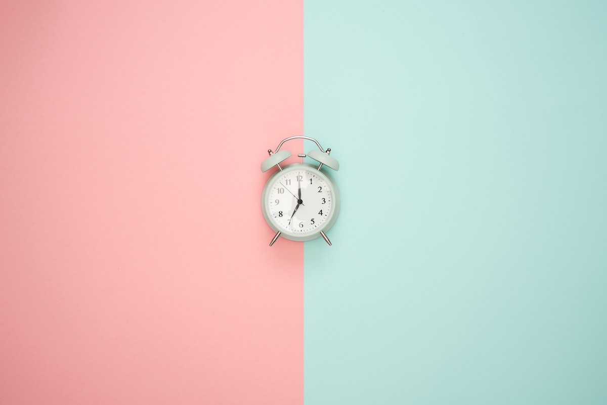 A photograph an old fashioned alarm clock on a pink and blue background by Moose Photos via Pexels